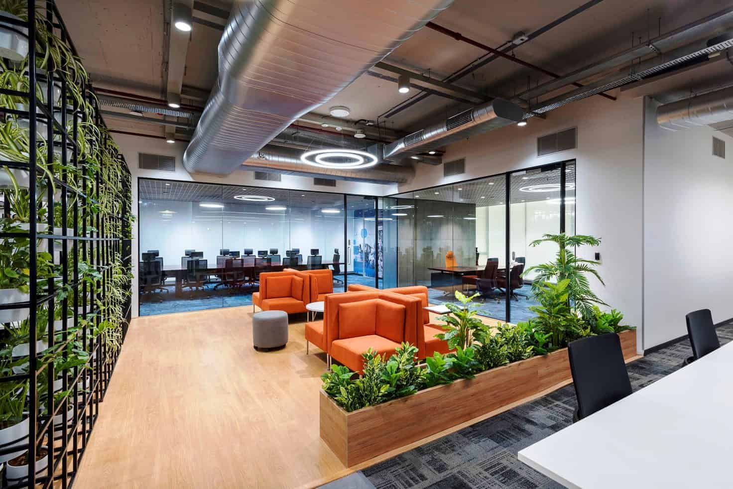 Modern office interior with contemporary furniture, green plants, glass walls, and innovative lighting for a stylish workspace.