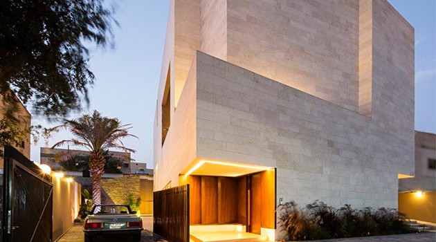 Modern minimalist beige stone house with clean lines and contemporary architectural design, illuminated by warm outdoor lighting, set in a lush landscape environment.