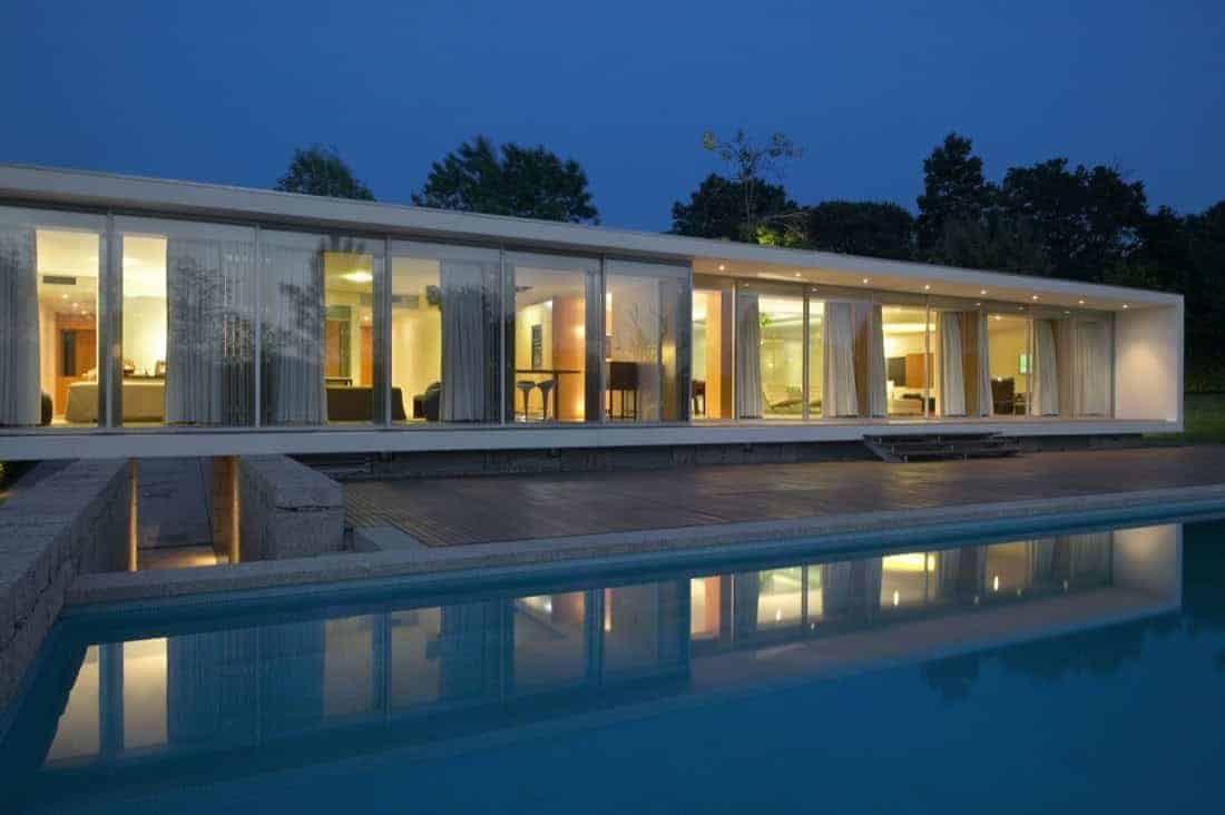 Modern luxury glass house with floor-to-ceiling windows, outdoor pool, and contemporary architectural design at dusk.