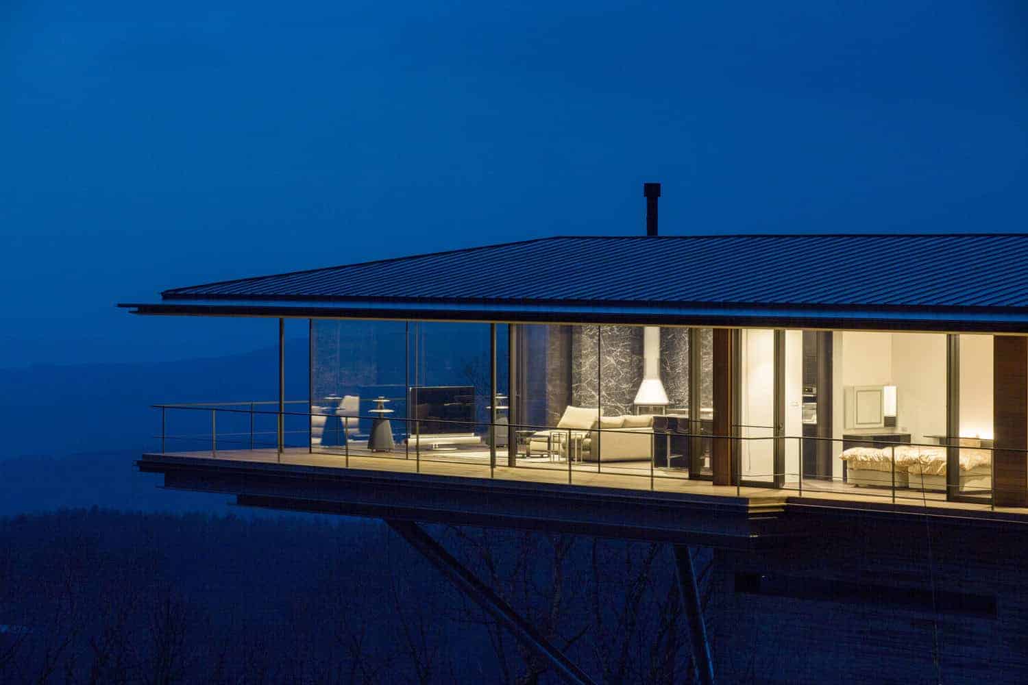 Stunning modern house with glass walls and an outdoor balcony, illuminated at night, showcasing contemporary architecture and innovative design.