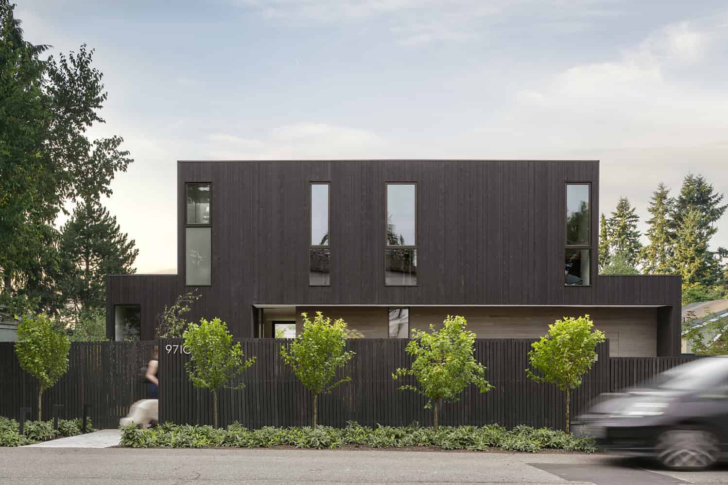 Contemporary modern house with dark wood exterior, sleek design, large windows, surrounded by lush greenery, showcasing modern architecture and innovative residential design.