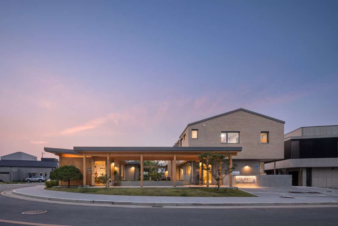 Contemporary modern architecture building with wood and concrete materials, featuring sleek design elements, large windows, and a landscaped surrounding under a twilight sky.