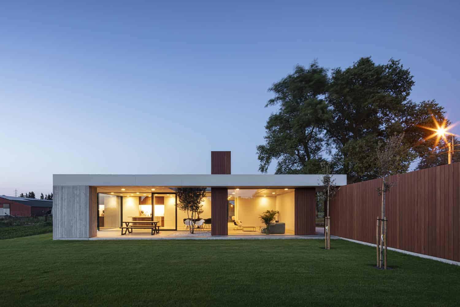 Modern minimalist house with open-concept design, large glass windows, and sleek architecture, surrounded by lush green lawn and wooden fencing, ideal for contemporary residential architecture.