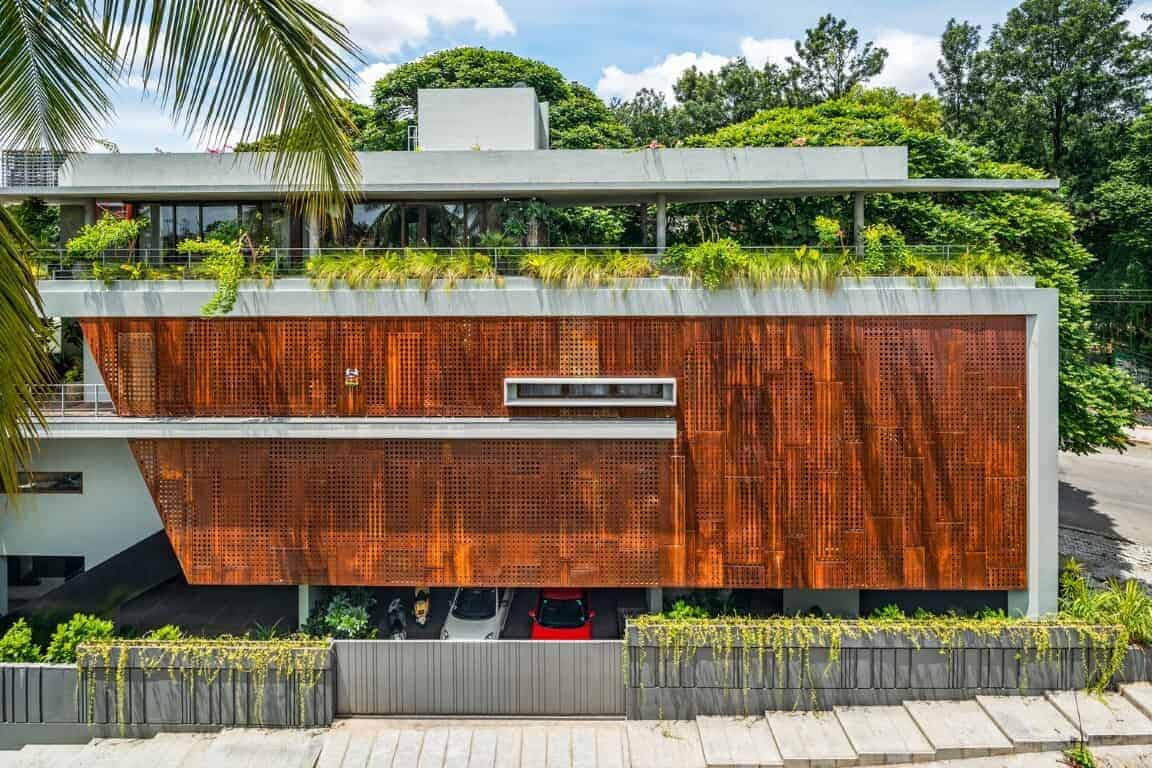 Contemporary modern house with rust-colored metal facade and lush green rooftop garden, surrounded by tropical trees, showcasing innovative architectural design and eco-friendly features.