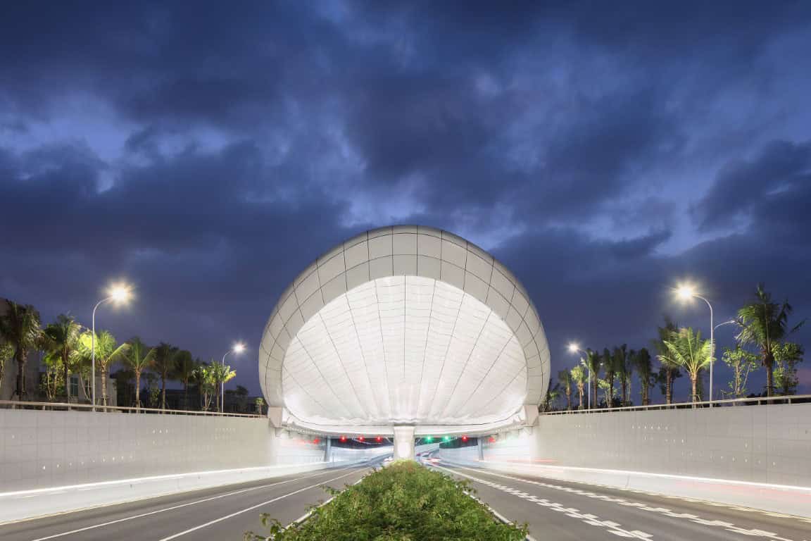 Futuristic tunnel entrance with modern architectural design, illuminated at night with palm trees lining the roadway, showcasing innovative architecture art designs and urban infrastructure.