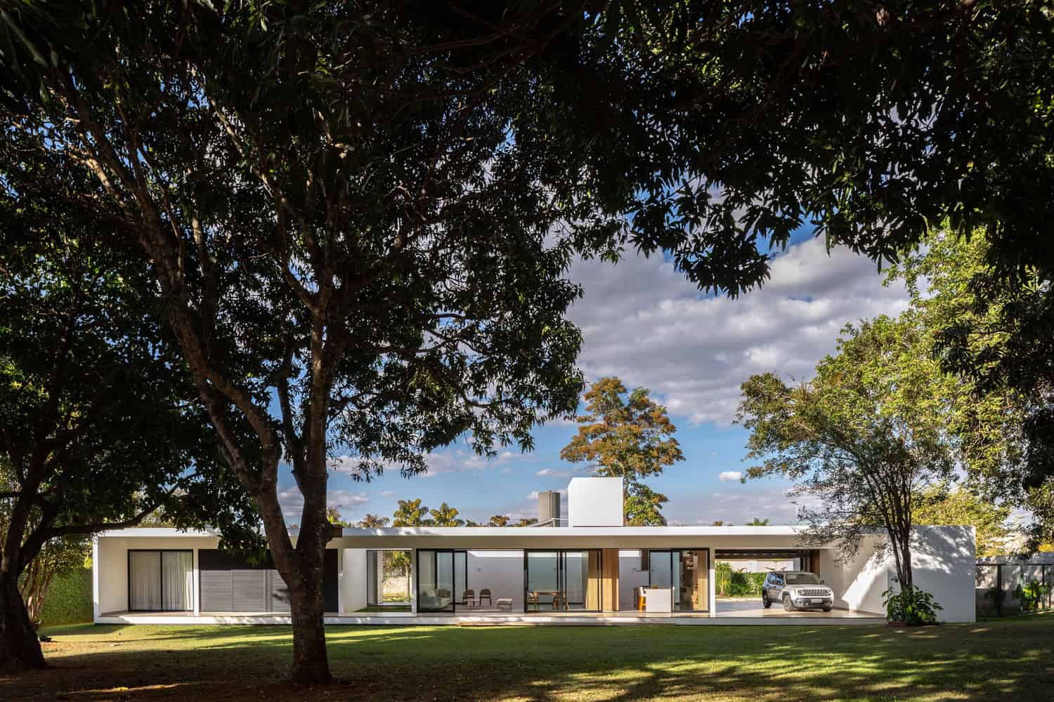 Contemporary modern house with minimalist design, large glass windows, flat roof, and landscaped garden surrounded by mature trees, showcasing sleek architecture and outdoor living spaces.