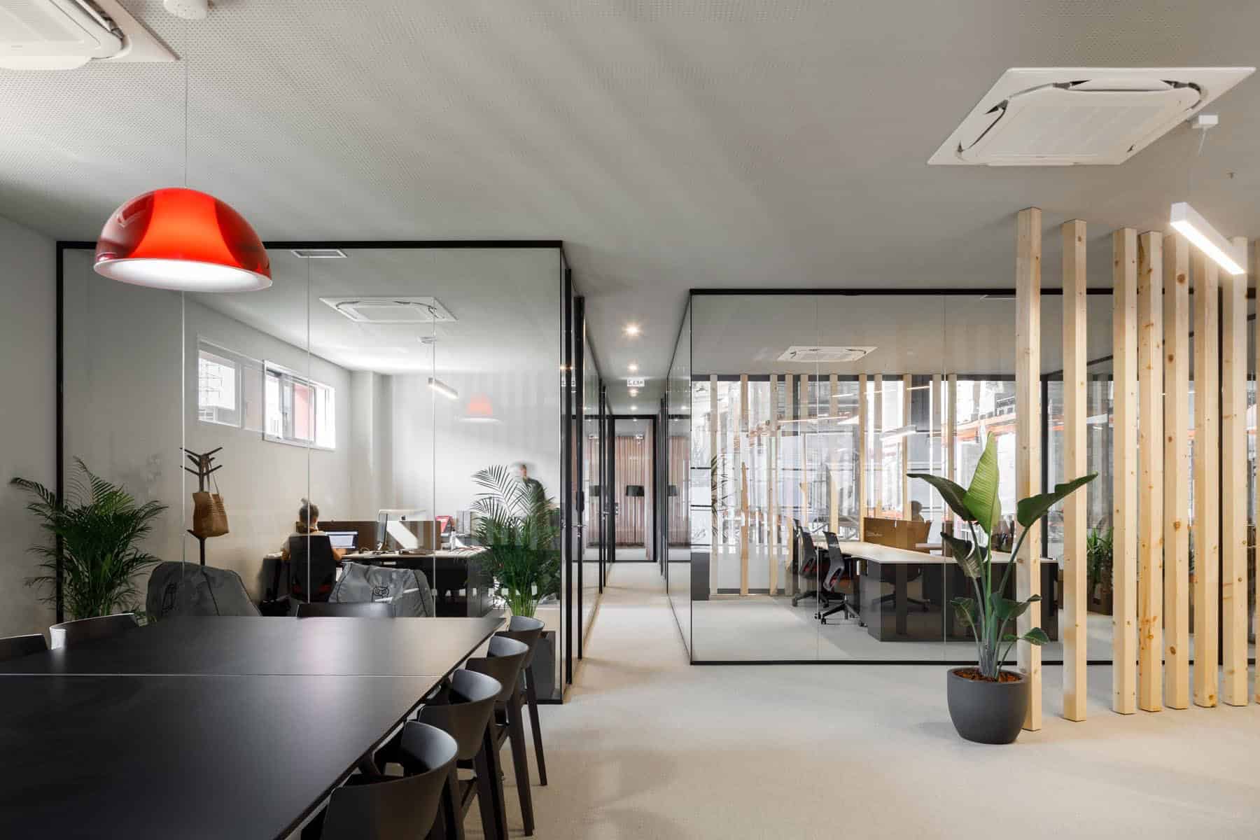 Modern office interior with glass partitions, natural lighting, indoor plants, and contemporary furniture showcasing innovative architecture and design elements.