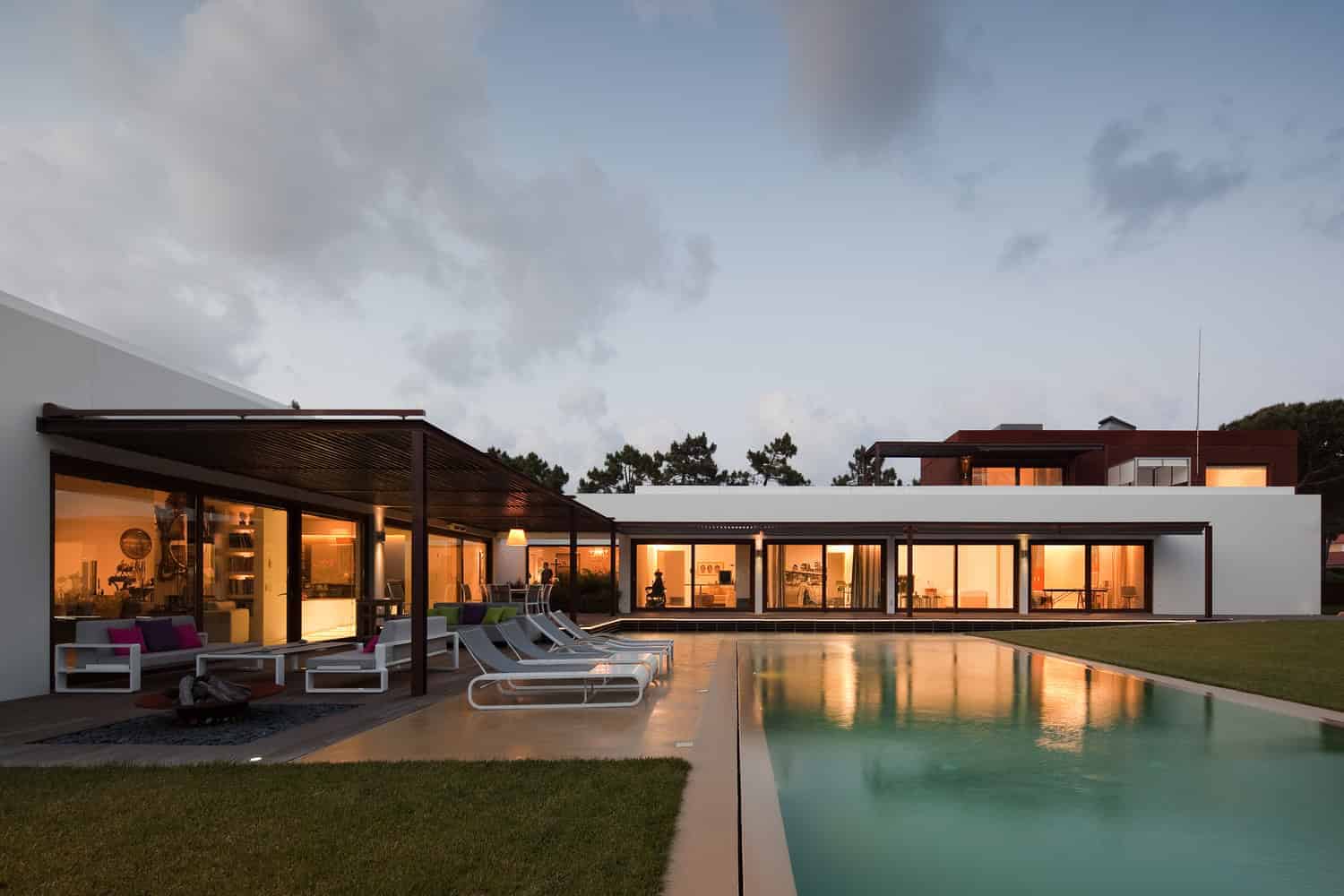 Modern minimalist house with outdoor pool and contemporary architecture at dusk, featuring sleek lines, large glass windows, and stylish outdoor furniture, emphasizing luxury home design and landscape architecture.