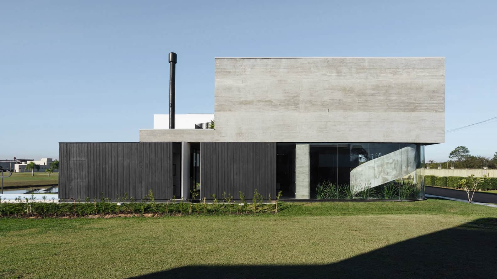 Modern minimalist house with concrete and black wood exterior, large glass windows, and a landscaped lawn, showcasing innovative architectural design and contemporary style.