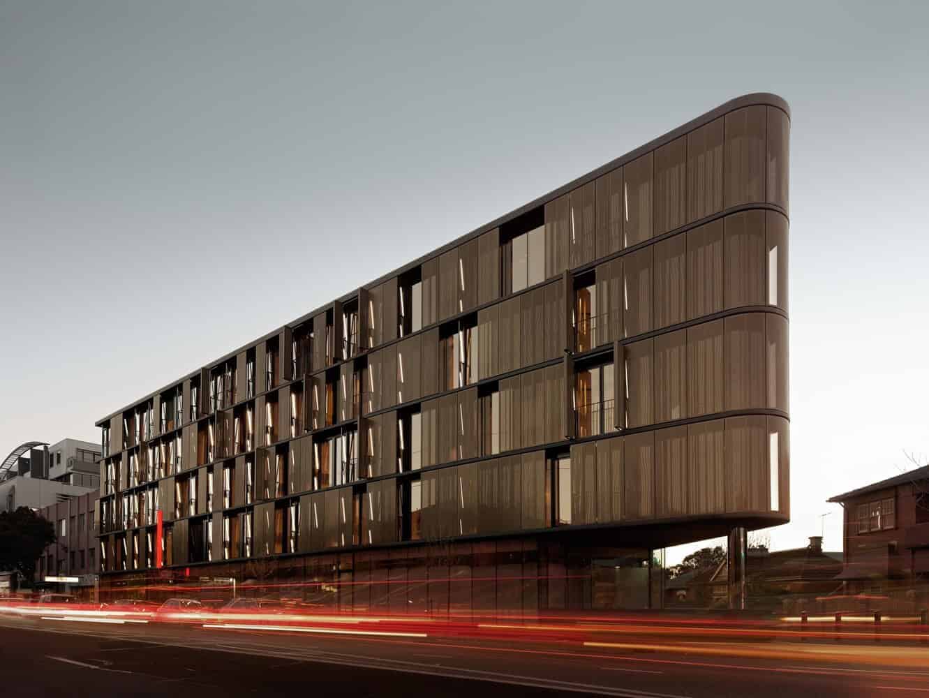 Contemporary modern hotel building with a sleek curved facade and vertical wooden slats, showcasing innovative architectural design in an urban setting.