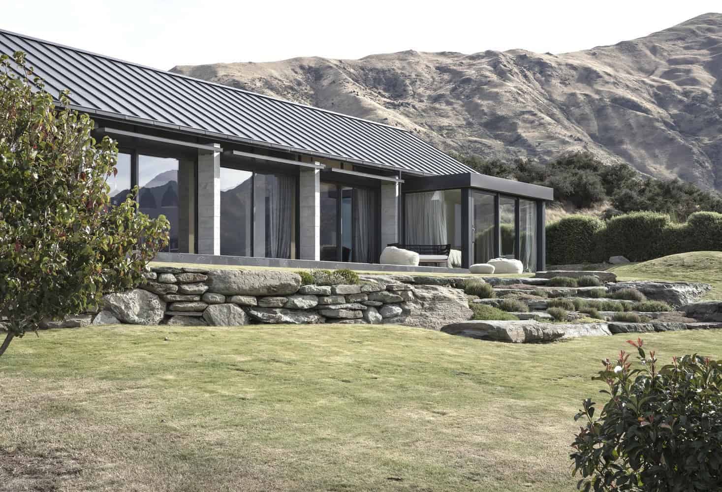 Contemporary modern house with large glass windows, stone accents, and a landscaped yard set against mountainous terrain for luxury residential architecture.