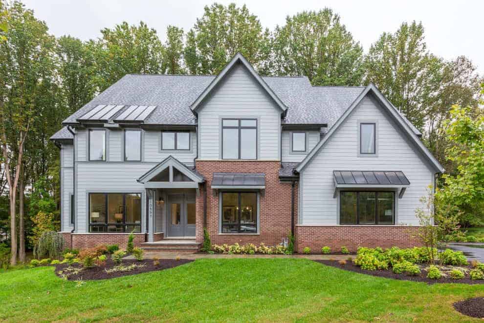 Modern Americana house with gray siding, brick accents, large windows, and landscaped front yard, showcasing contemporary architectural design and curb appeal.