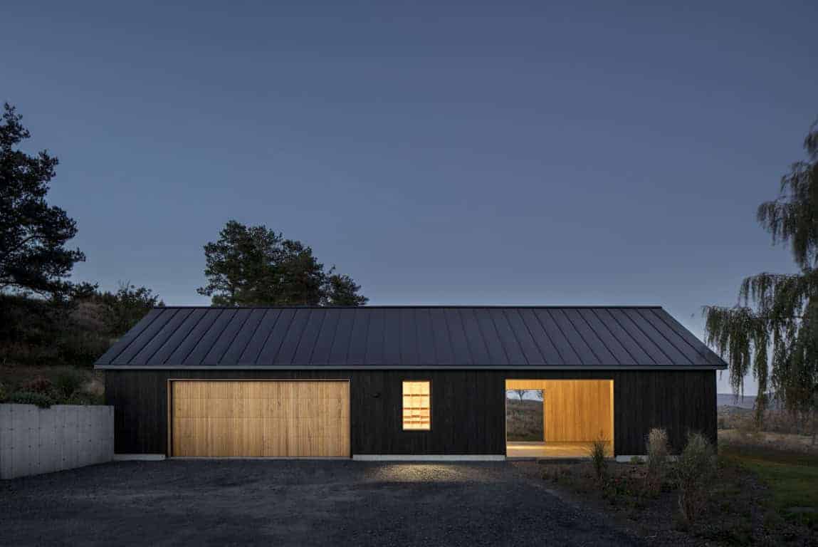 Modern barn-style home with black exterior and wooden accents, minimalist architecture, contemporary design, outdoor lighting, rural landscape, architecture art designs, eco-friendly construction.