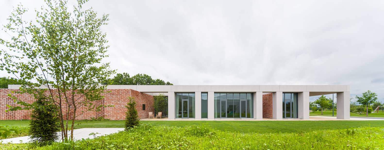 Contemporary modern house with clean lines and large glass windows, surrounded by lush green lawn and trees, showcasing minimalist architectural design and outdoor seating area.