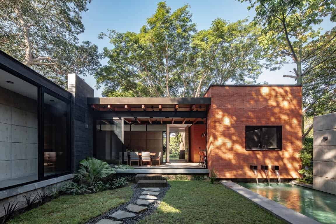 Modern minimalist house with a combination of brick, concrete, and glass materials, surrounded by lush greenery and designed for luxury outdoor living.
