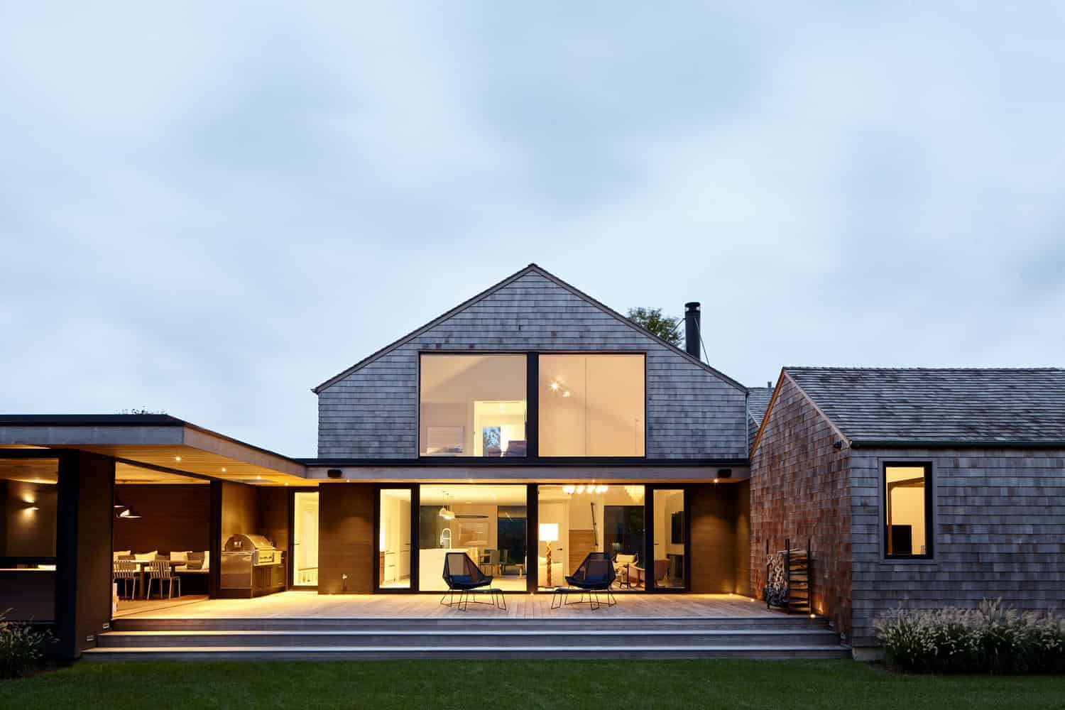 Modern contemporary house with wooden siding and large glass windows, illuminated at dusk, showcasing sleek architectural design and outdoor living space.