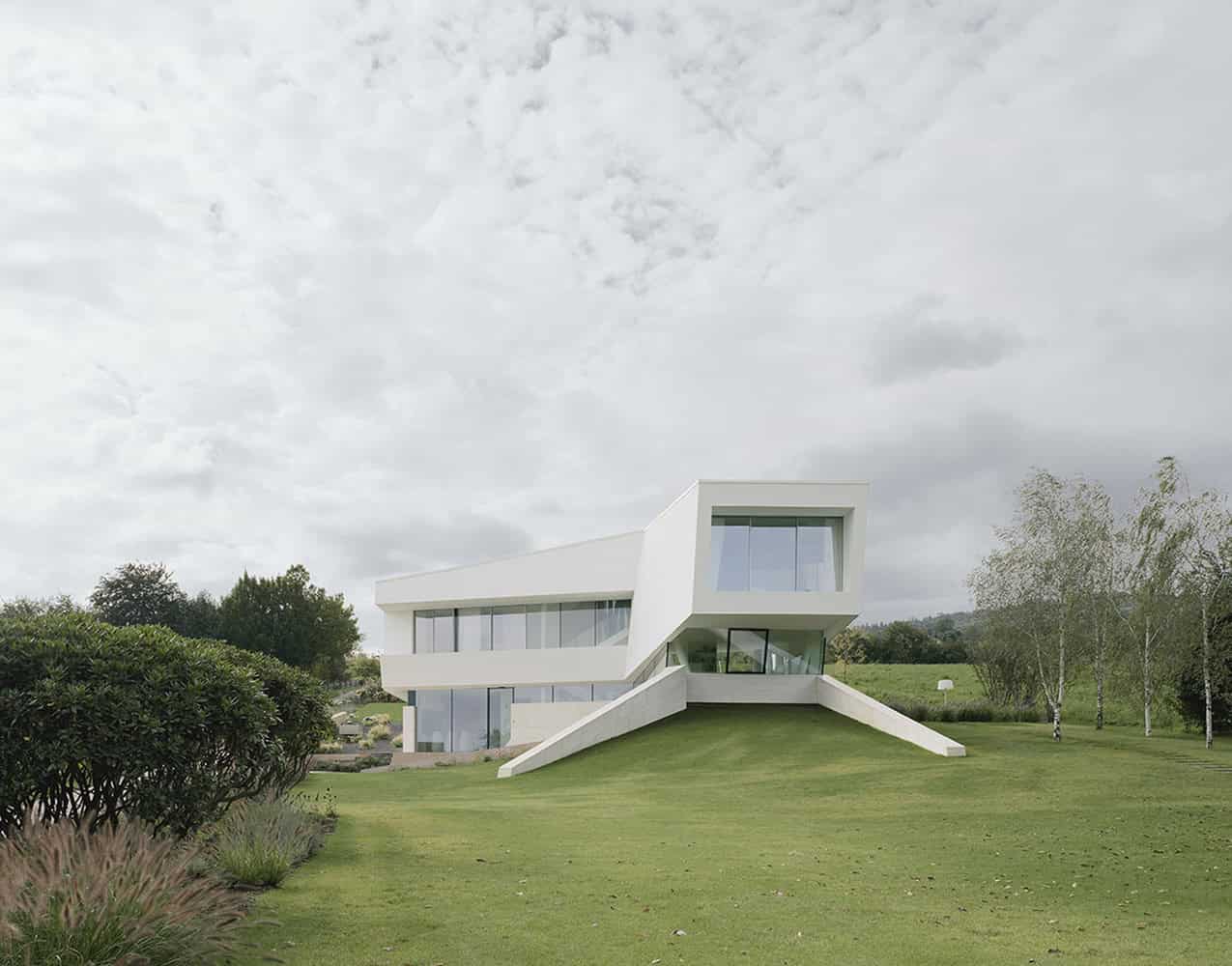 Contemporary white modern house with unique angular design and extensive glass windows on a landscaped green lawn.