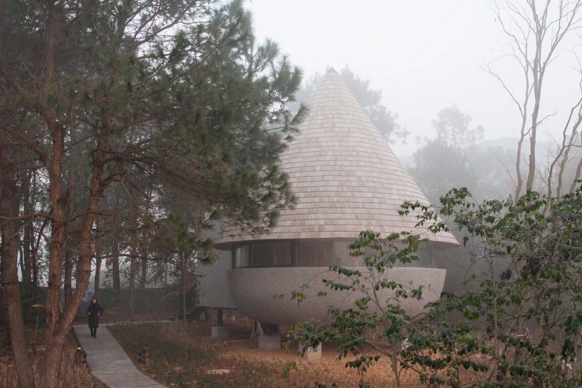 Futuristic modern house with a conical roof nestled among trees in a foggy forest setting, showcasing innovative architecture and organic design elements.