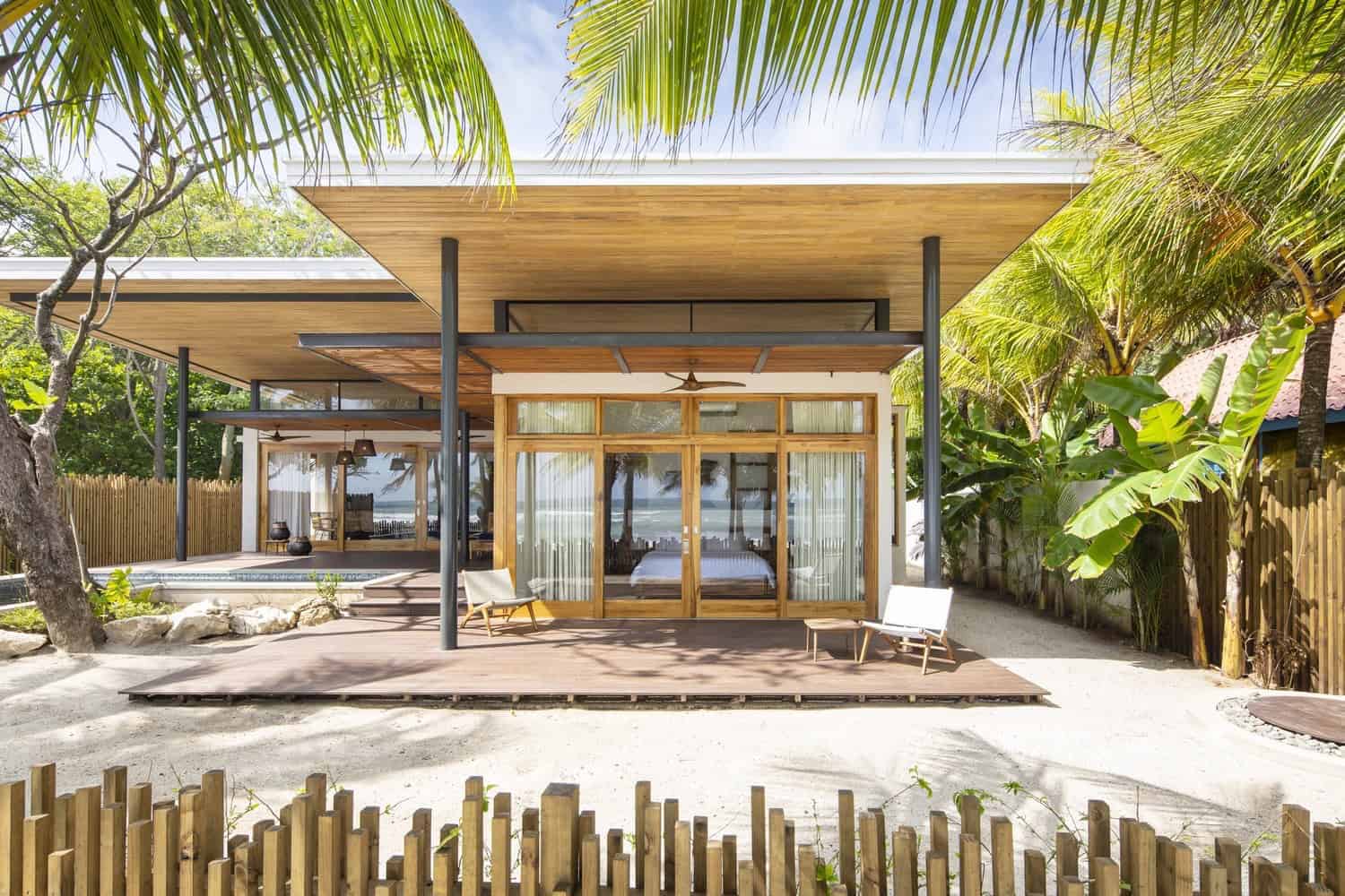 Modern tropical beach house with open-concept design, wood accents, large glass doors, and lush landscaping. Perfect for seaside living and outdoor relaxation.