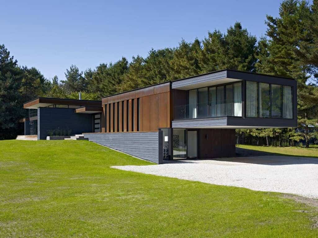 Modern contemporary house with large glass windows, sleek black and wooden exterior, situated in lush green surroundings, showcasing stylish architecture and innovative design.