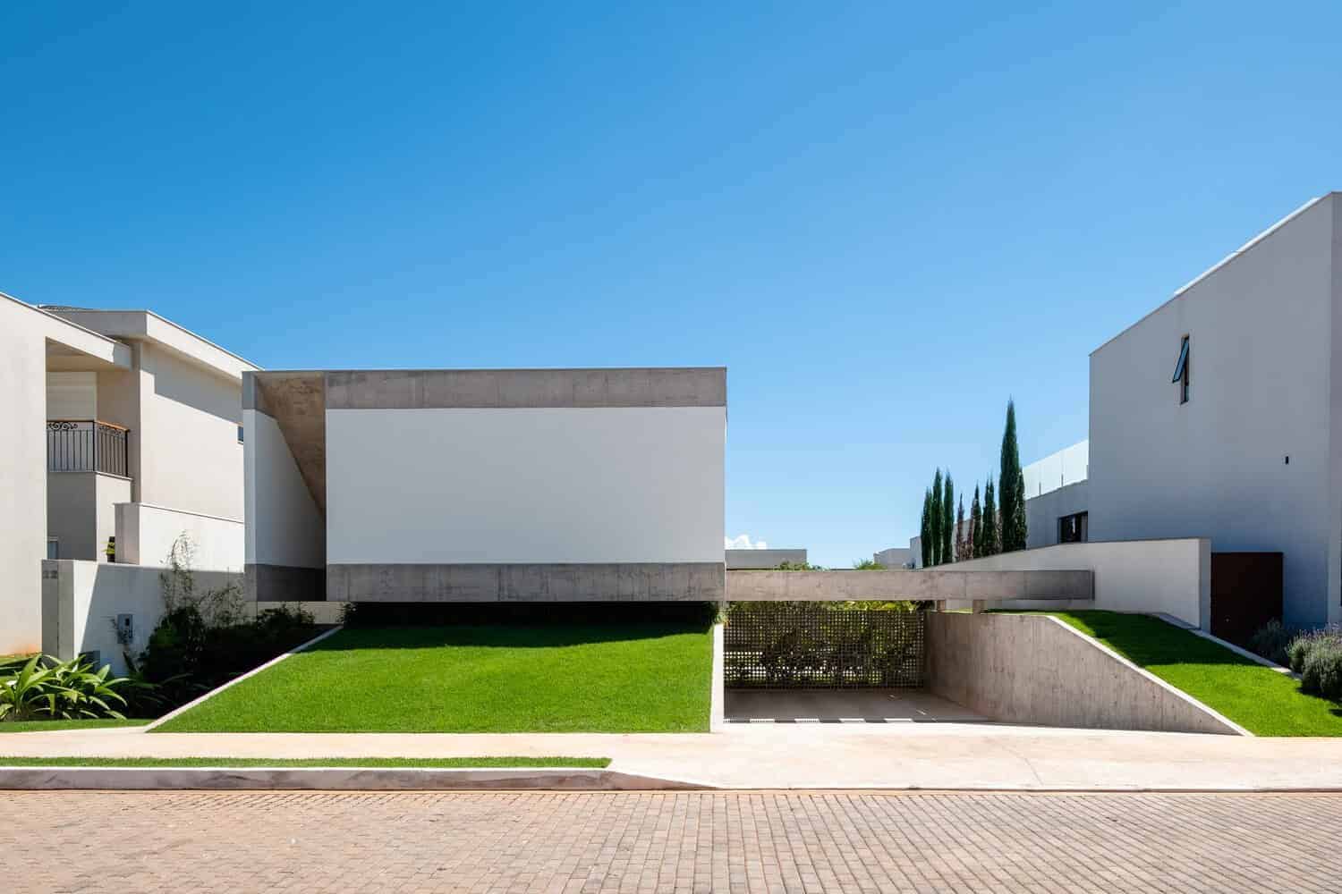 Contemporary minimalist residential architecture with clean lines, white walls, and landscaped lawn, showcasing modern design and curb appeal in a sunny suburban setting.