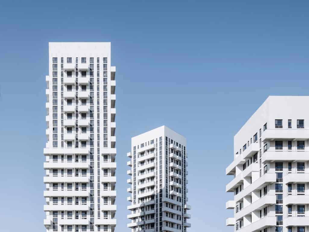 Luxury modern white high-rise apartment buildings with geometric design against a clear blue sky.