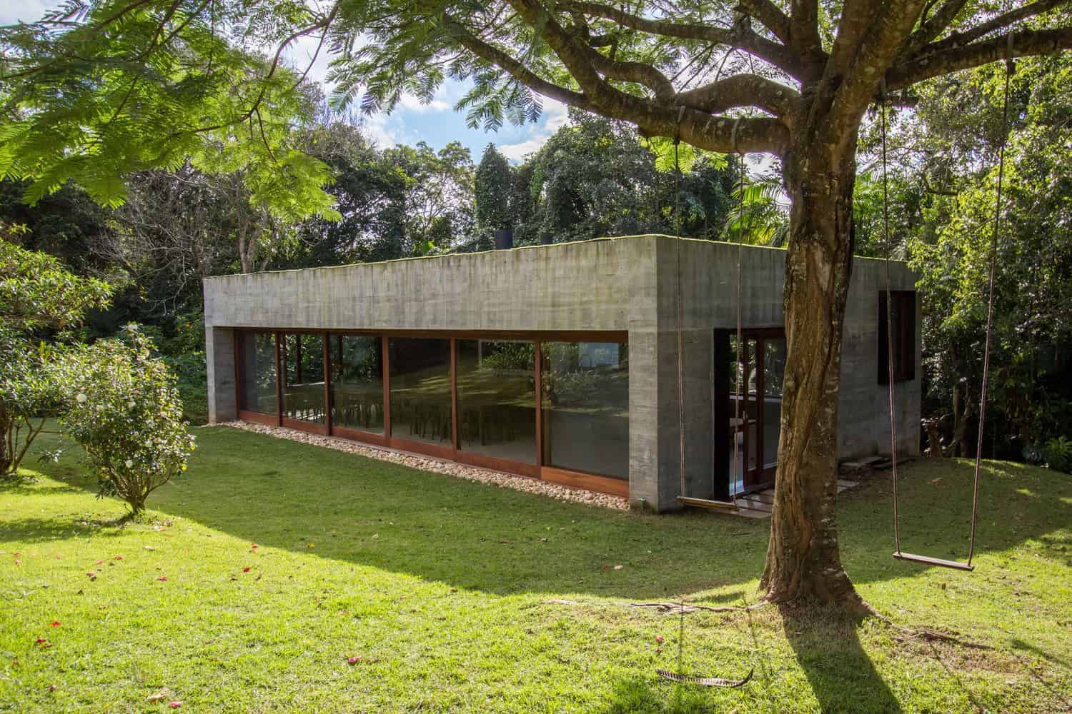 Modern concrete house with large glass windows nestled in lush green garden, minimalistic architectural design, eco-friendly residence, surrounded by mature trees and vibrant landscaping, peaceful nature retreat.