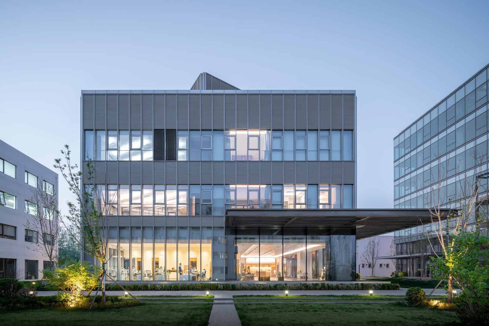 Modern glass office building with sleek architecture and open interior spaces, surrounded by landscaped gardens and illuminated at dusk, exemplifying innovative corporate architecture and contemporary design.