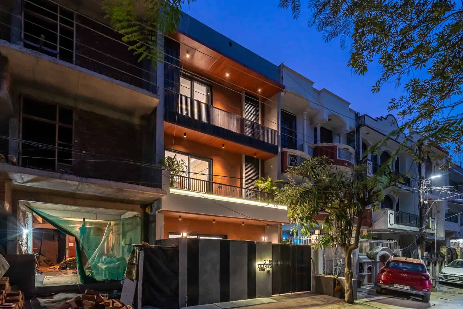 Contemporary urban building facade featuring modern architectural design elements with balconies, lighting, and mixed materials in a city street scene at dusk.