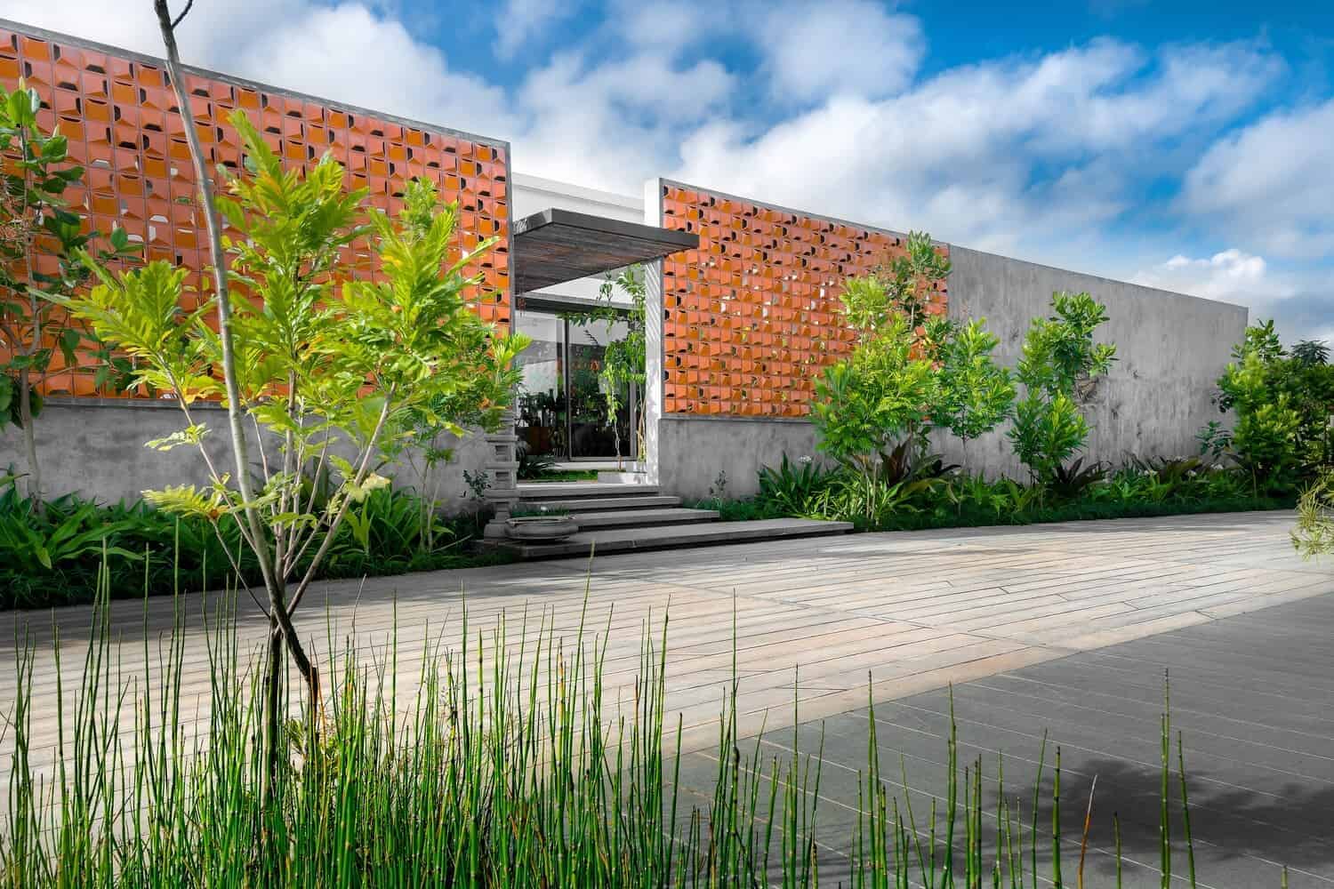 Modern minimalist house with concrete walls and decorative brick panels, lush landscaping, and a stone pathway, showcasing innovative architecture and contemporary design.