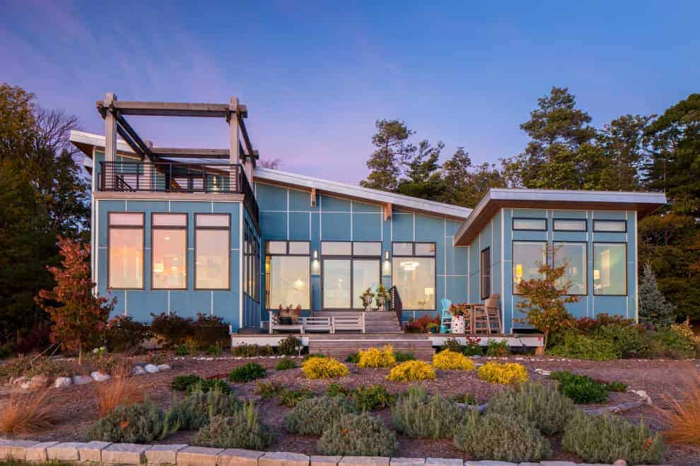 Modern blue architectural home with large windows and a landscaped garden, showcasing innovative design and stunning exterior architecture.
