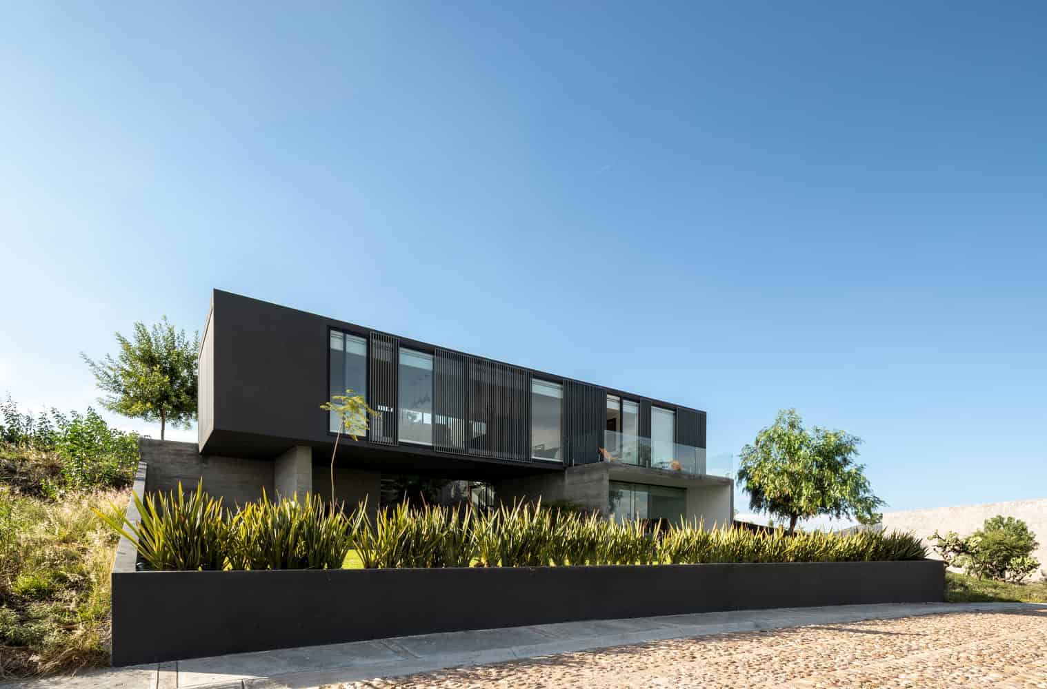 Modern black and glass residential house with contemporary architecture and innovative design elements, set against a clear blue sky.