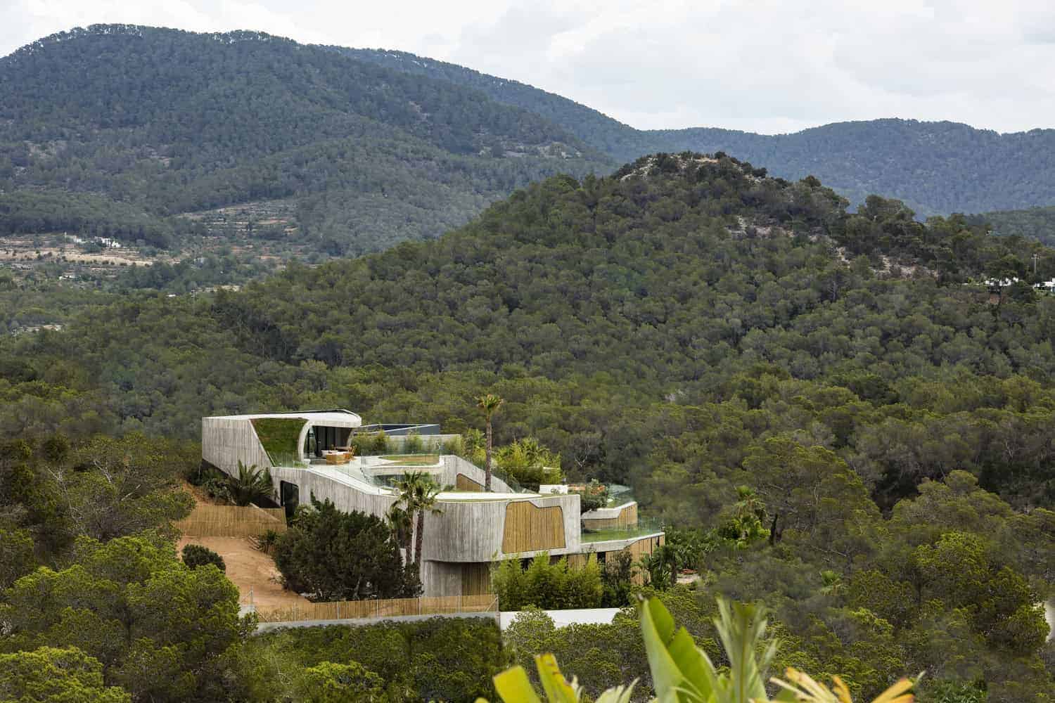 Modern hillside luxury home with innovative architecture surrounded by lush green mountains, emphasizing contemporary design and integration with natural landscape.