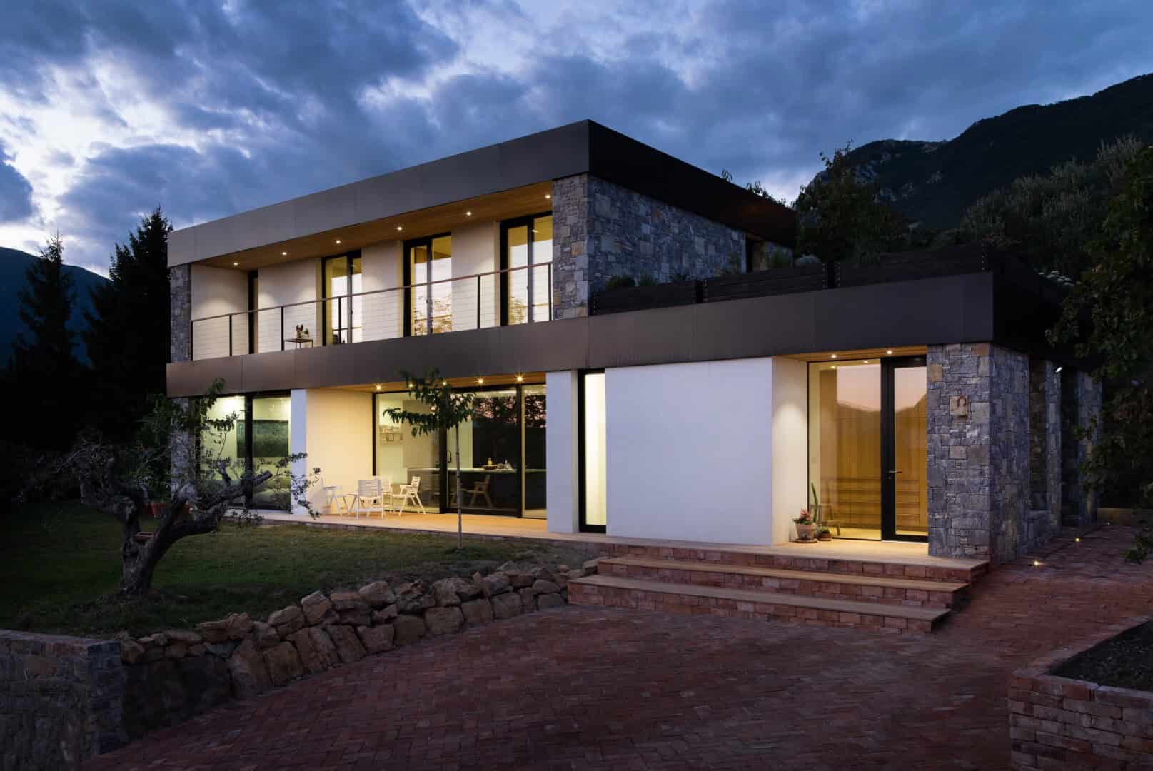 Contemporary modern house with large glass windows, stone accents, and spacious balconies set against mountain scenery, showcasing innovative architecture and stylish design.
