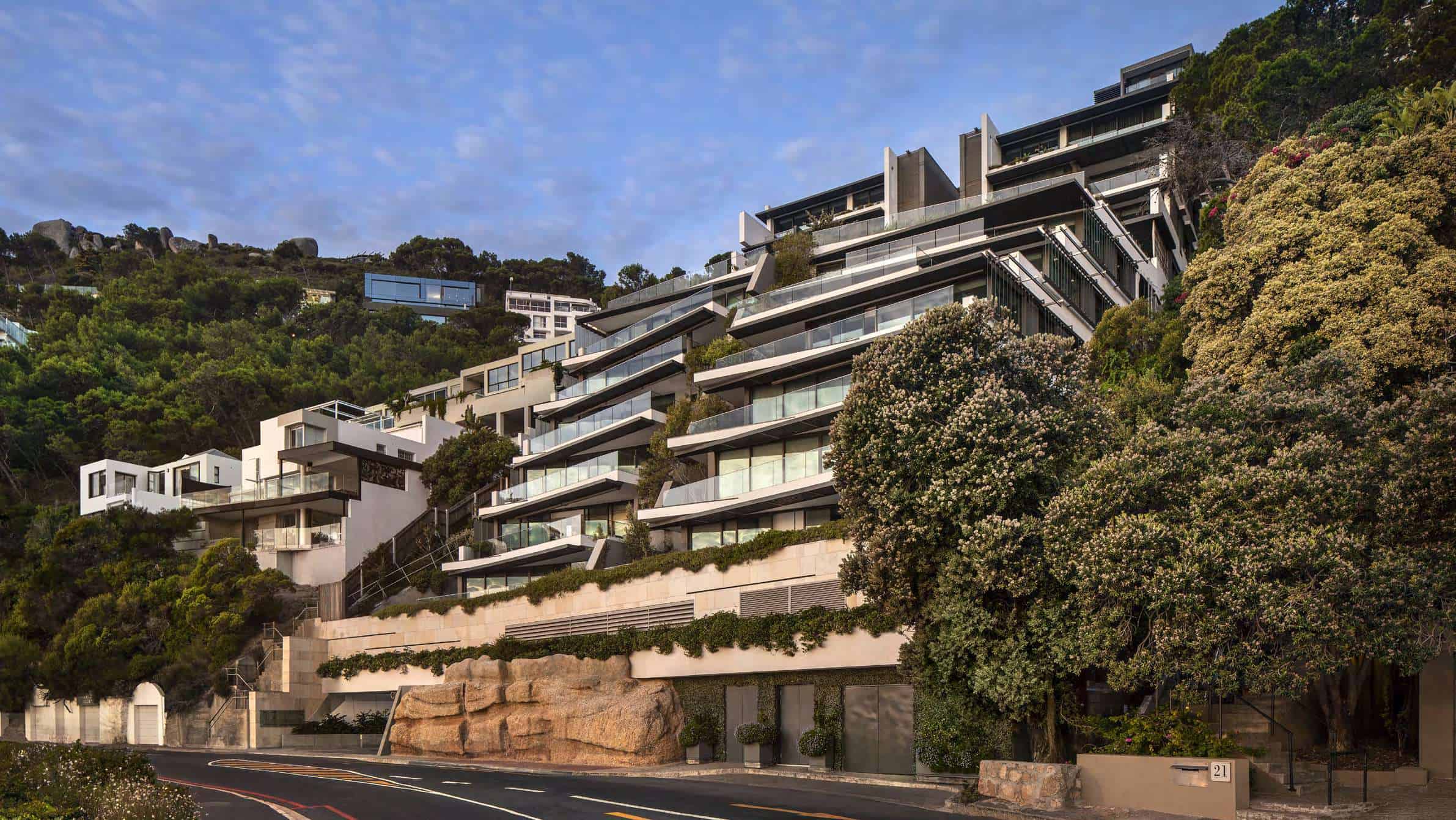 Luxury modern hillside residential building with expansive glass balconies and landscaped greenery, showcasing contemporary architecture and hillside living design.