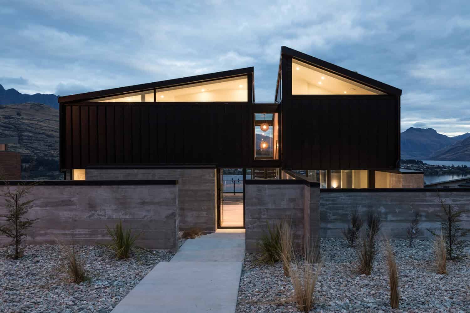Contemporary modern house with unique angular architectural design, black exterior, large glass windows, scenic mountain view at dusk, minimalist landscaping.