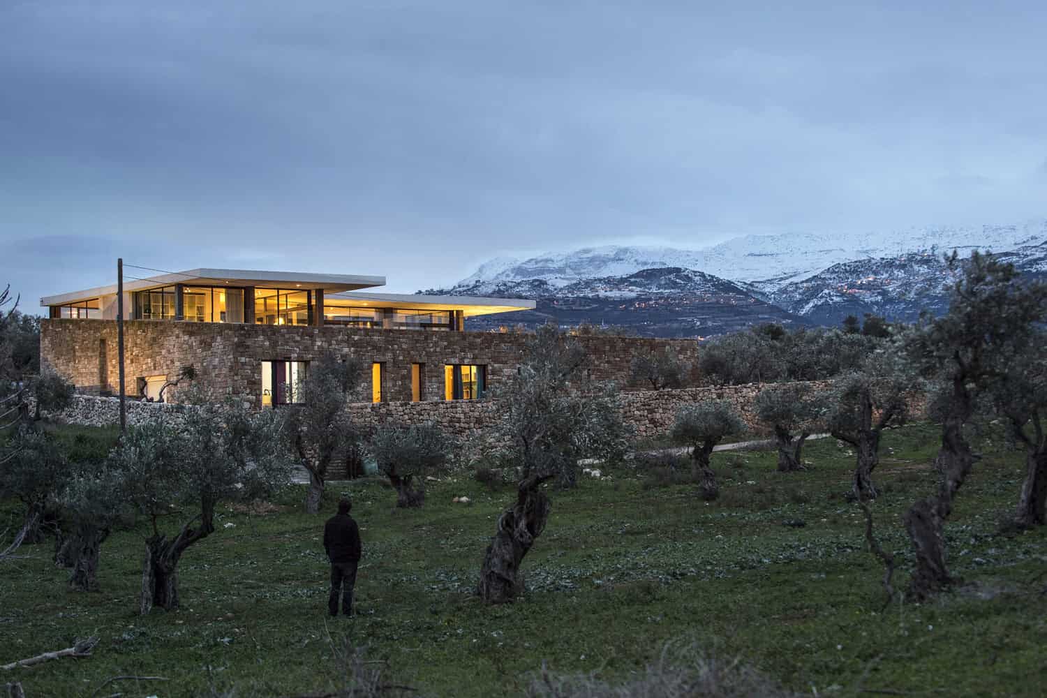 Modern contemporary house with large glass windows and stone accents in a scenic mountainous landscape.