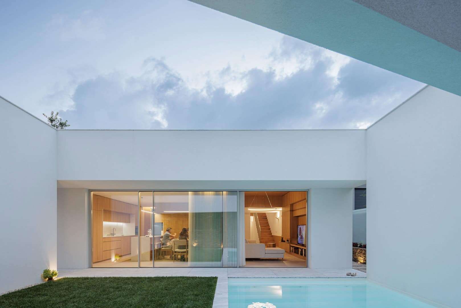 Contemporary minimalist house with modern interior design, open plan living space, wooden accents, and seamless glass doors overlooking a private pool.