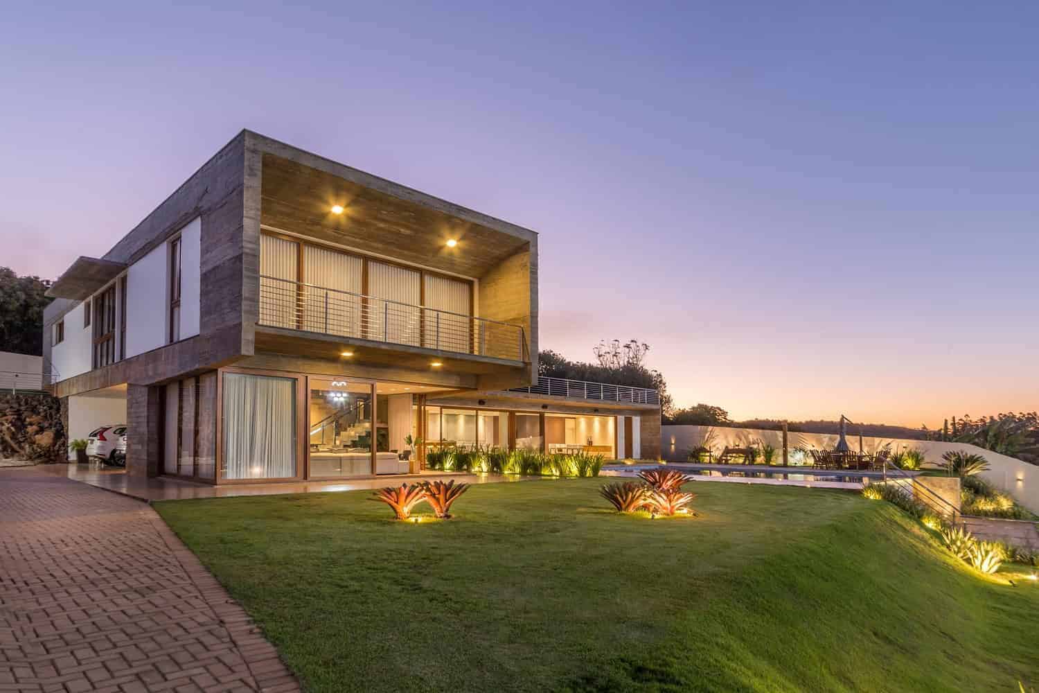 Contemporary modern house with sleek architecture, large glass windows, and outdoor lighting, set against a sunset sky. Features spacious terraces, lush garden, and a pool area for luxury living.