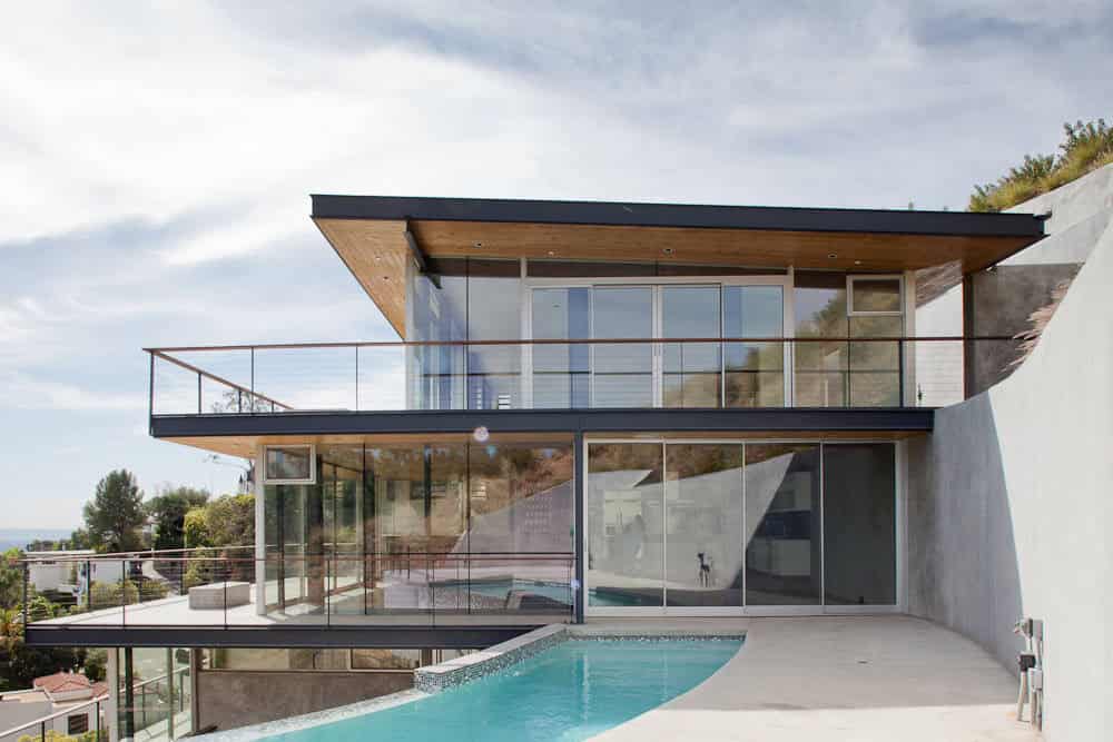 Contemporary modern house with large glass windows and spacious balconies, featuring a sleek design, outdoor pool, and hillside views, exemplifying innovative architecture and stylish residential interior design.