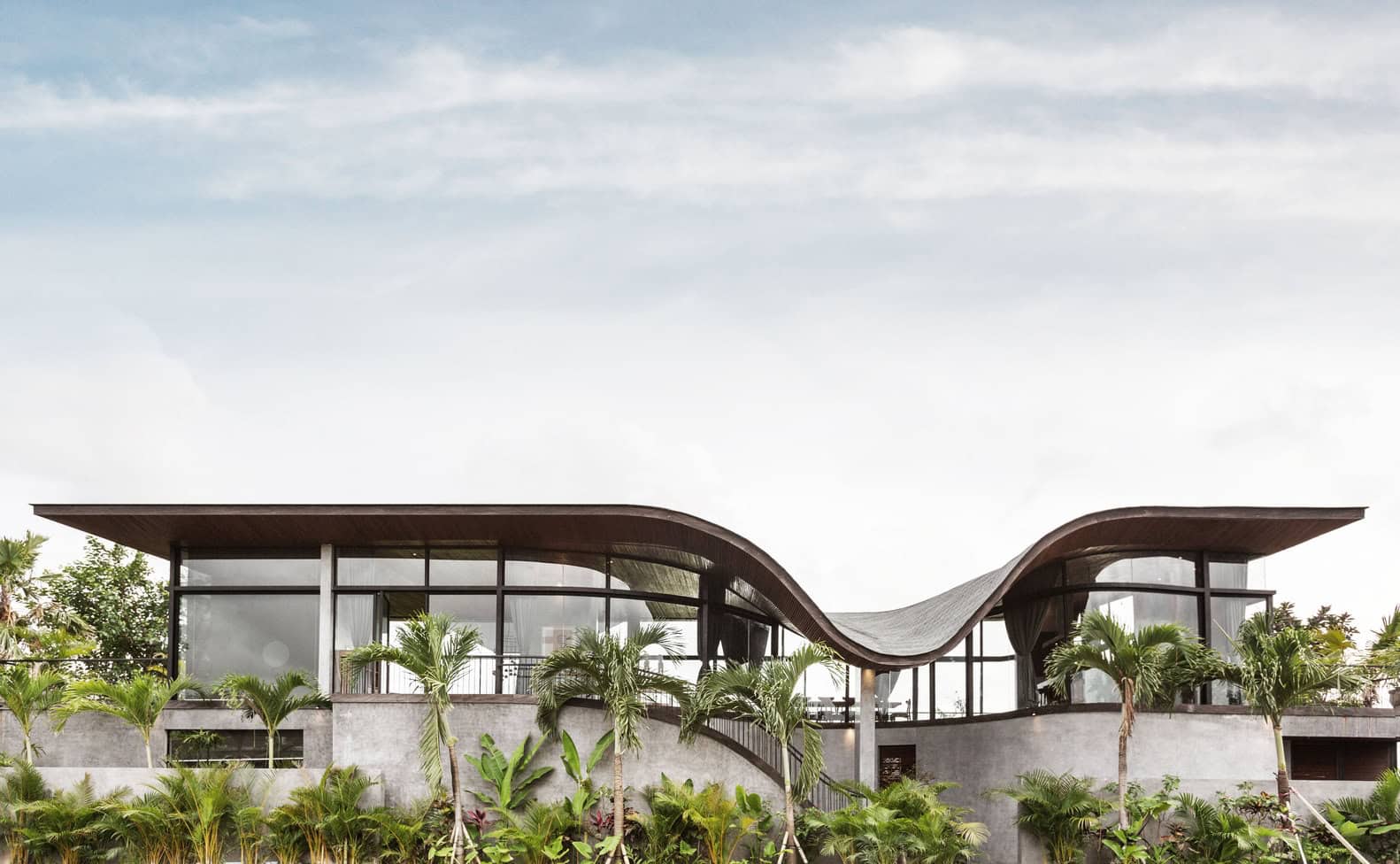Futuristic modern house with curved roof and large glass windows, lush tropical greenery, and minimalist concrete structure, showcasing innovative architectural design and eco-friendly style.
