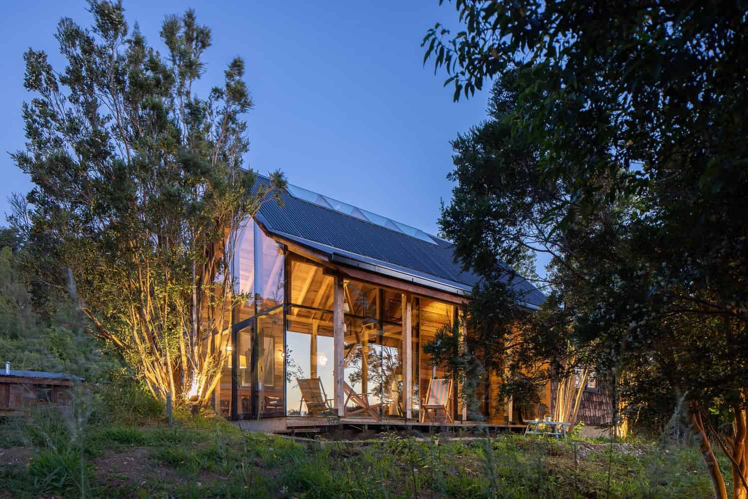 Sustainable modern house with glass walls and wooden accents nestled in a lush forest setting during twilight.