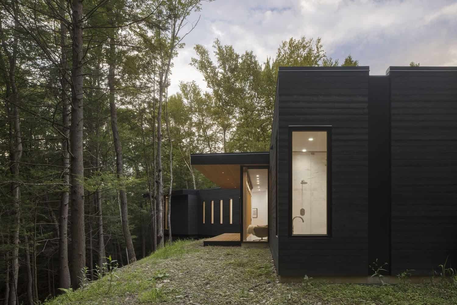 Contemporary black modern house with large glass windows nestled in a dense forest setting. Modern architecture emphasizing sleek design, natural surroundings, and innovative use of materials.