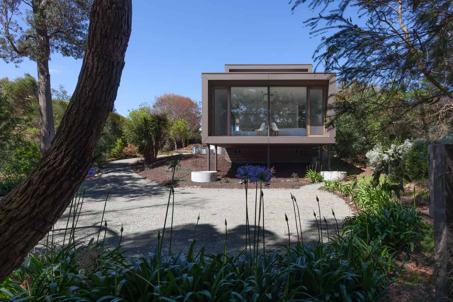 Modern minimalist hillside house with large glass windows and contemporary design, seamlessly blending with natural surroundings.