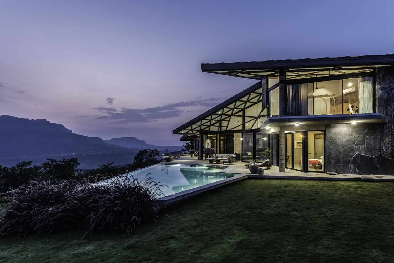 Modern luxury house with a stunning infinity pool overlooking mountain views at dusk, featuring contemporary architecture, large glass windows, and elegant outdoor lounging areas.