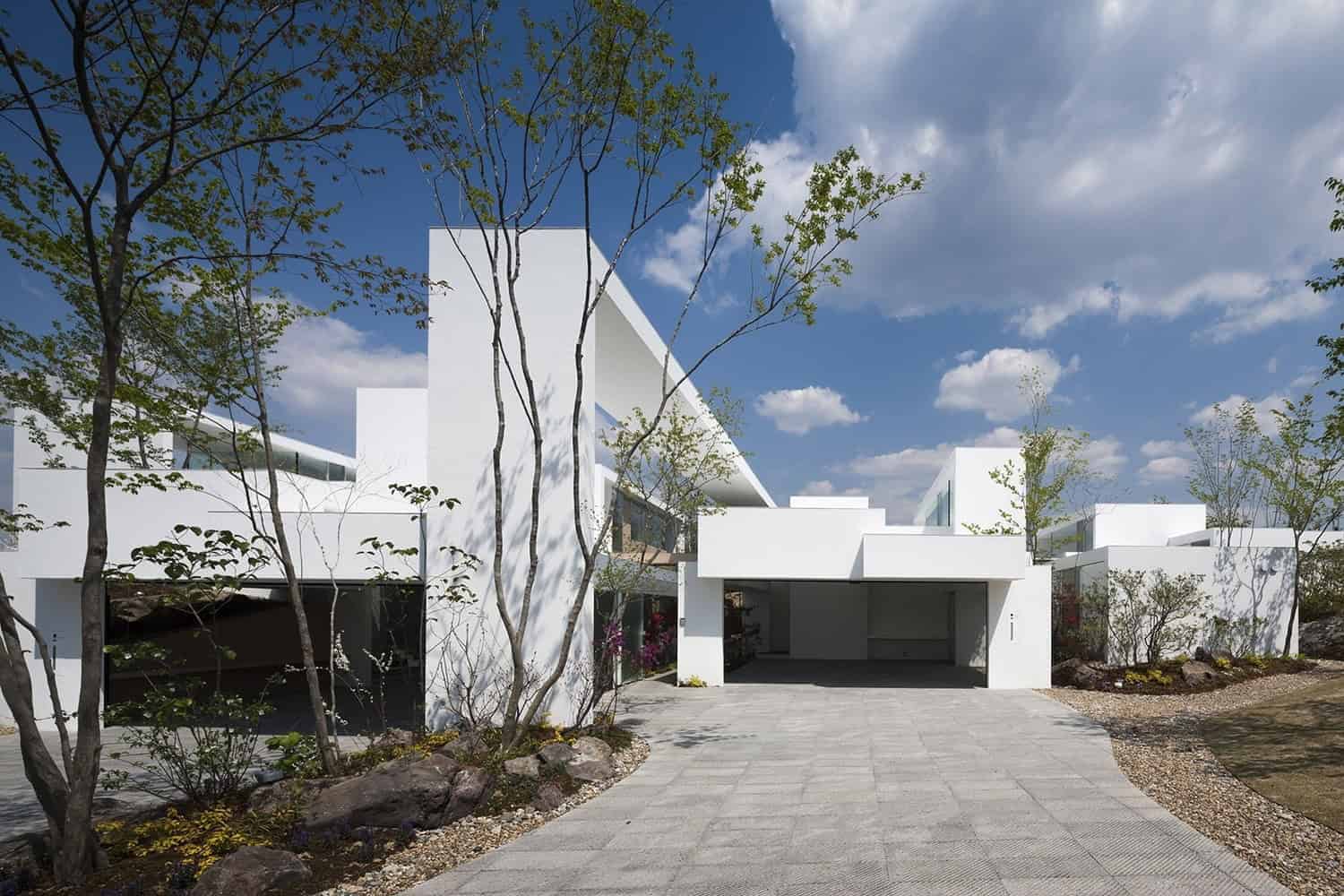 Modern minimalistic white house exterior architecture with clean lines and geometric design, landscaped driveway, and trees under a blue sky with clouds, showcasing contemporary architecture art designs.