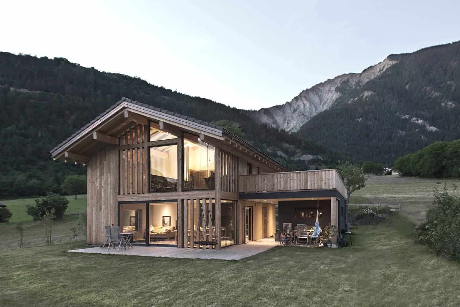 Modern wooden house with large glass windows surrounded by lush green landscape and mountain views, showcasing contemporary architecture and sustainable design.