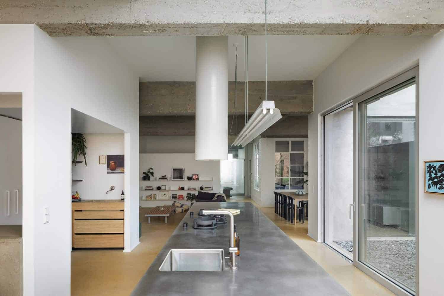 Modern minimalist kitchen with concrete ceiling, sleek gray countertop, and large sliding glass doors offering natural light and an indoor-outdoor connection.