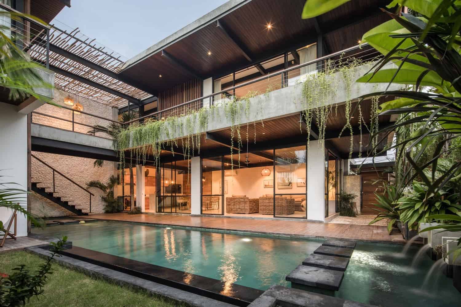 Modern tropical villa with outdoor swimming pool, lush greenery, and contemporary architecture featuring raw concrete, wood accents, and glass elements for a luxurious open-air living space.