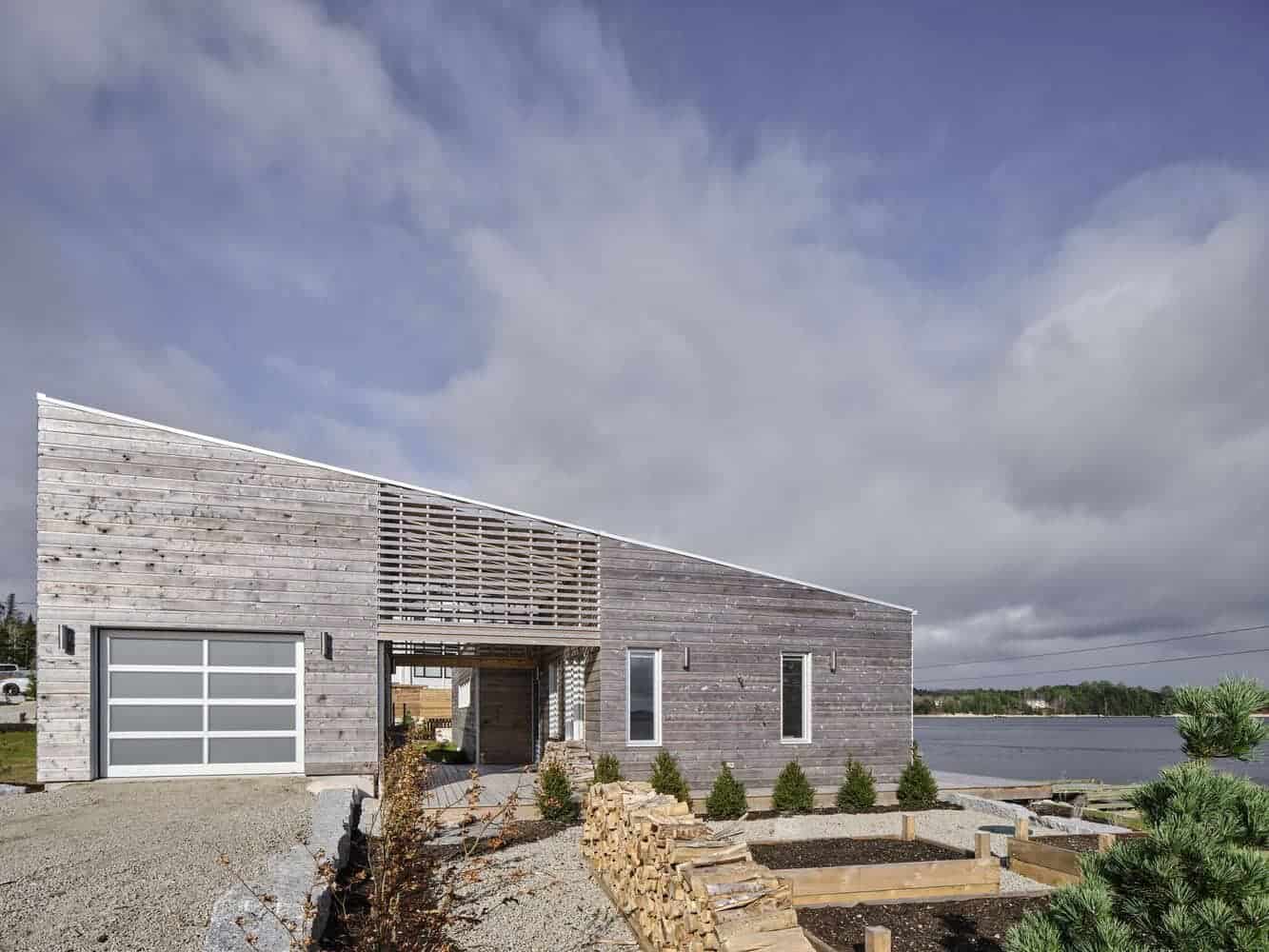 Modern lakefront house with contemporary architectural design, wooden exterior finish, large windows, and outdoor landscaping in a scenic waterside setting.